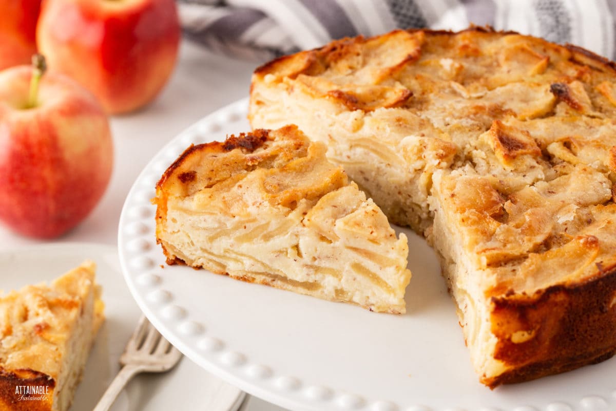 apple cake on a white plate with a wedge of cake adjacent.