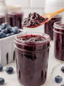 wooden spoon scooping blueberry jam out of a canning jar.