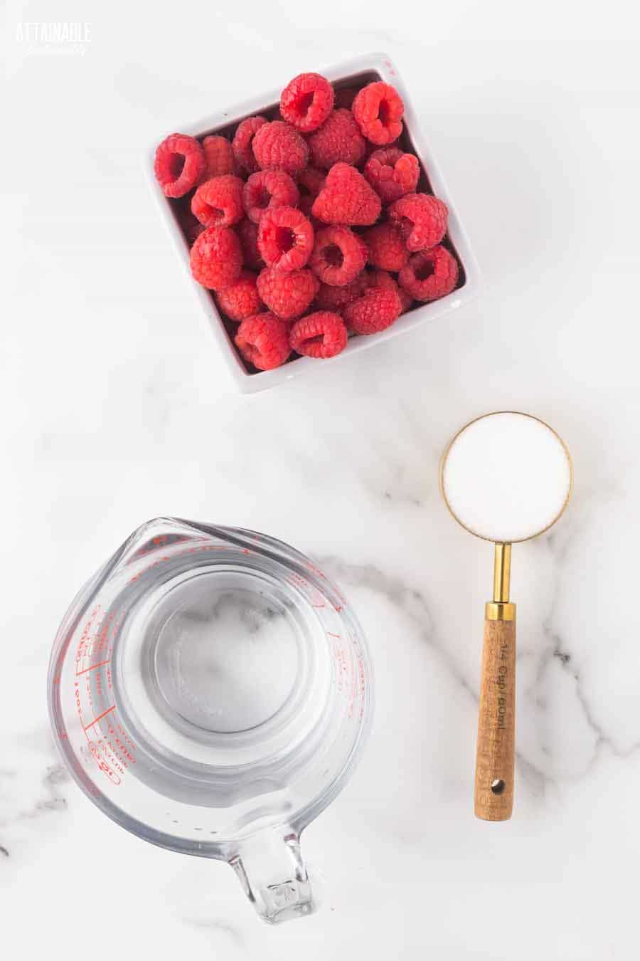 box of raspberries, measuring cup of water, sugar in a wooden handled measuring cup.