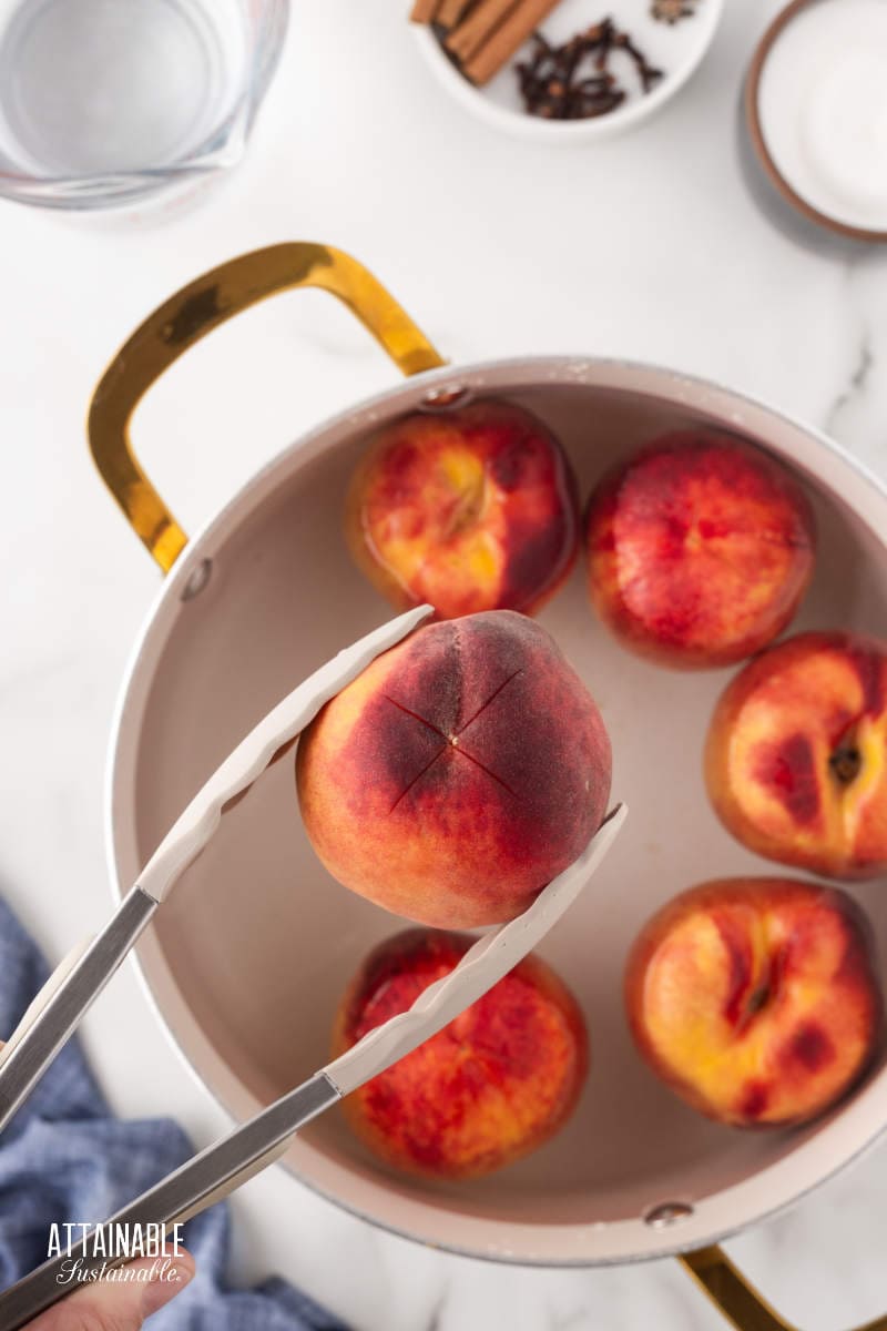 tongs holding a peach over a pot of water.