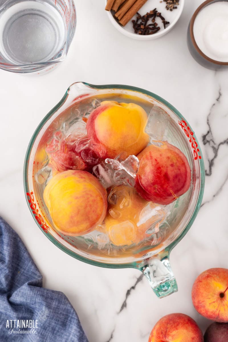 peaches floating in a large measuring cup of ice water.